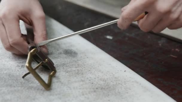 Primer plano de hombre curtidor con delantal utiliza un destornillador para la artesanía de un cinturón de cuero marrón en el taller de cuero. Proceso de trabajo del cinturón de cuero en el taller de cuero . — Vídeos de Stock