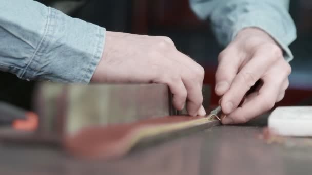 Um artesão de couro está cortando as bordas de um cinto. O mestre está usando uma ferramenta de borda chanfrada . — Vídeo de Stock