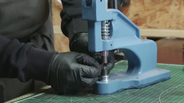 Gros plan de l'homme tanneur dans des gants noirs utilise une presse pour installer des raccords métalliques. Processus de travail dans l'atelier de cuir .