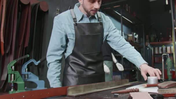 Der professionelle Gerber legt in der Werkstatt Kleister auf einen Gürtel. Arbeitsprozess des Ledergürtels in der Lederwerkstatt. — Stockvideo