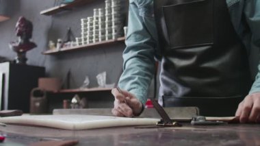 Önlüklü profesyonel tabakçı deri atölyesinde yeni bir kahverengi deri kemer yapıyor. Deri atölyedeki deri kemerin çalışma süreci..