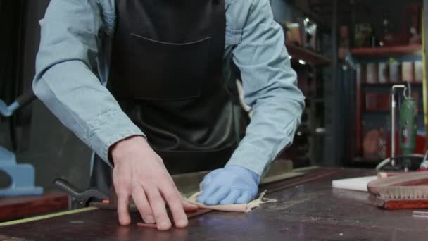 Un artesano de cuero frota los bordes de un cinturón. El maestro está usando la herramienta de frotar . — Vídeos de Stock