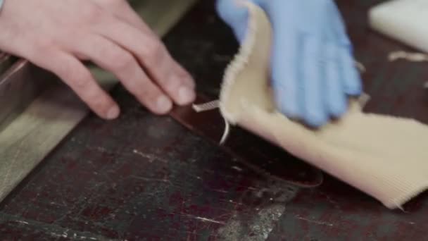 Un artesano de cuero frota los bordes de un cinturón. El maestro está usando la herramienta de frotar . — Vídeo de stock