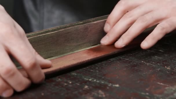 Fechar-se do bronzeador profissional o homem põe a pasta em um cinto na oficina. Processo de trabalho da correia de couro na oficina de couro . — Vídeo de Stock