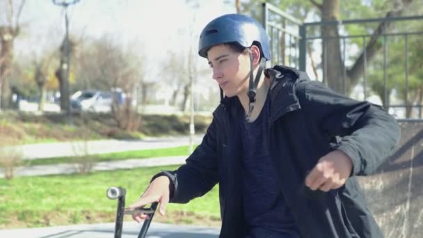 Молодий гонщик bmx сидить на велосипеді і розмовляє на спартанському телефоні — стокове відео