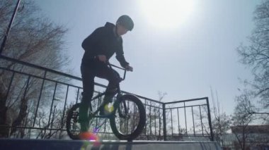 Genç bir BMX sürücüsü kaykay parkında rampalara biniyor.