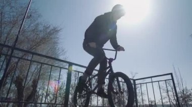 Genç bir BMX sürücüsü rampadan geçiyor ve kaykay parkında numaralar yapıyor.