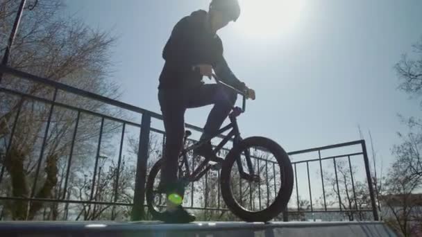 Молодой велосипедист делает трюки в экстремальном парке на закате — стоковое видео