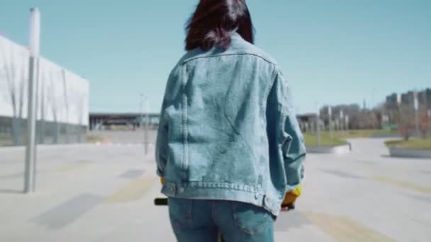 Achteraanzicht van jonge aziatische vrouw in een jeans jas rijdt een scooter in de zomer park — Stockvideo