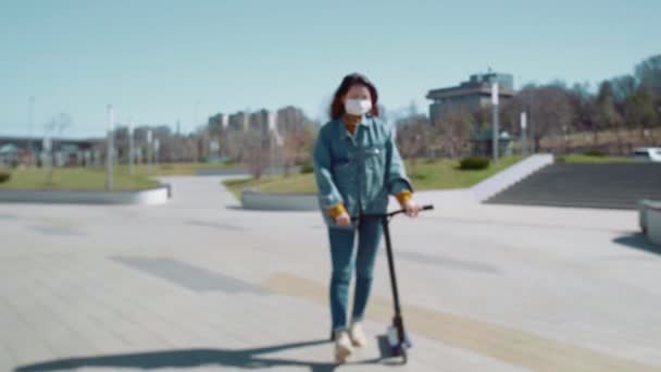 Joven asiática mujer en médico máscara paseos con kick scooter en verano parque — Vídeo de stock