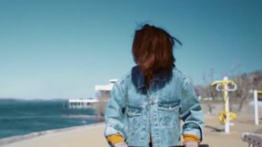 Kot ceketli genç Asyalı kadın nehir kıyısında scooter kullanıyor.