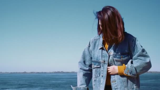 Ung asiatisk kvinna i jeans jacka promenader med skotern och tar selfies i en sommarpark nära floden — Stockvideo