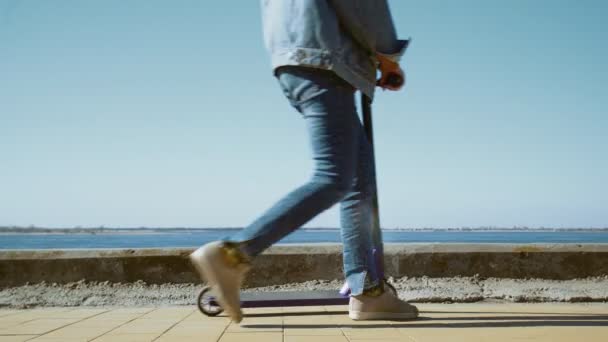 Jovem mulher asiática em uma jaqueta jeans e máscara médica senta-se na fronteira com a scooter perto do rio — Vídeo de Stock