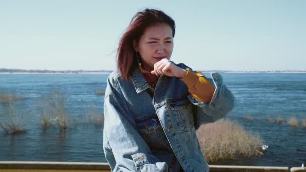 Junge asiatische Frau in einer Jeansjacke hustet und geht aus — Stockvideo