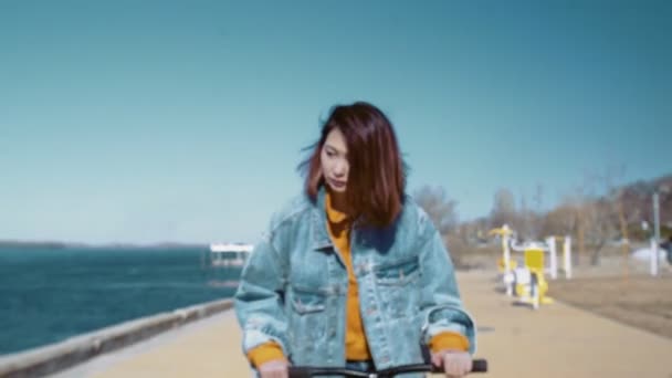 Jonge aziatische vrouw in een jeans jas rijdt de scooter in de buurt van de rivier — Stockvideo