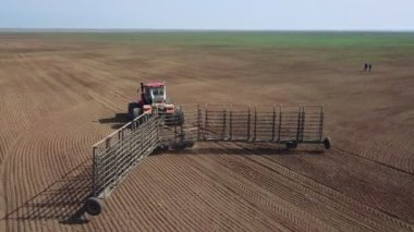 Tarlalarda arazi hazırlayan traktördeki bir çiftçinin hava görüntüsü. Beyaz traktör tarlaları sürüyor, toprağı ekime hazırlıyor..