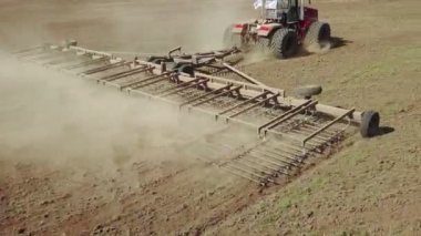 Büyük bir kanca kuvvetiyle enerji dolu güçlü bir traktörün hava görüntüsü, sonbaharda kış ekinleri için bir disk ekiciyle ekin ekiyor.