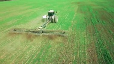Tarlalarda arazi hazırlayan traktördeki bir çiftçinin hava görüntüsü. Beyaz traktör tarlaları sürüyor, toprağı ekime hazırlıyor..