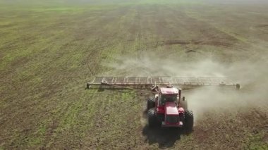 Büyük bir kanca kuvvetiyle enerji dolu güçlü bir traktörün hava görüntüsü, sonbaharda kış ekinleri için bir disk ekiciyle ekin ekiyor.