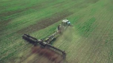 Bir traktörde tohum eken çiftçi tarlaya tahıl ekimi için toprağı hazırlıyor. Toz toprağına tohum ekiyorum. Bahar tarım işi. Hava görüntüsü, insansız hava aracı öne doğru uçar traktörü takip eder