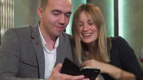 Genç ve güzel bir çift bir kafede buluşup akıllı telefondan fotoğraf izliyorlar. — Stok video