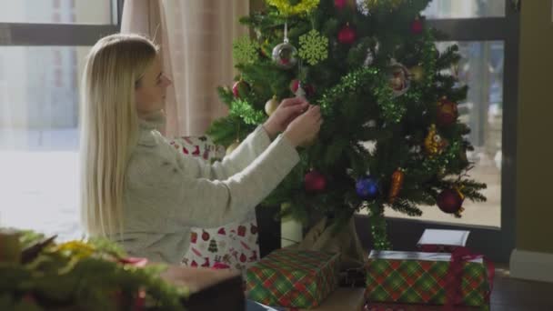 Menina bonita em suéter decora árvore de Natal por bolas amarelas. Belo interior de Natal . — Vídeo de Stock