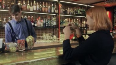 Gülümseyen barmen içki dolduruyor ve barda neşeli bir ziyaretçiyle konuşuyor.