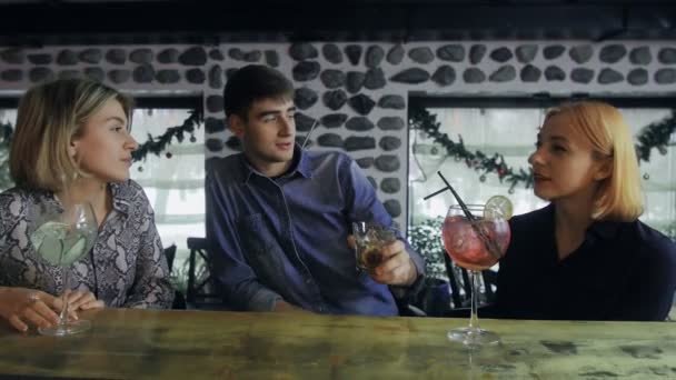 Due donne e un uomo sono seduti al bancone del bar e bevono cocktail. — Video Stock