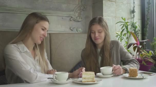 Deux belles jeunes femmes buvant du café et mangeant des gâteaux au café — Video