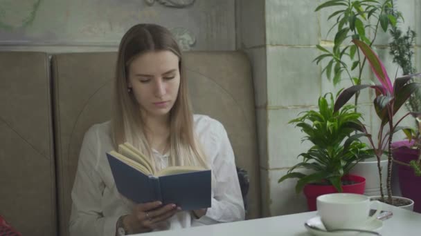 Junge, schöne Mädchen lesen Buch im Café — Stockvideo