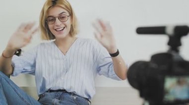 Genç bayan blogcu kamerada konuşuyor ve eliyle selam veriyor.