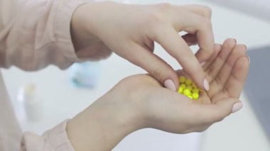 Bir sürü küçük ve sarı hap tutan genç bir kadın, ağzına bir hap alıyor ve ellerini Corona 'nın altına koyuyor. Covid 19