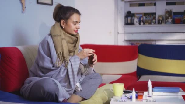 Mujer joven con un terrón tomar pastillas tomar té sentado en casa en el sofá se siente mal — Vídeos de Stock