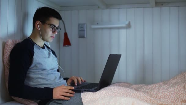 Jeune homme travaillant sur ordinateur portable au lit dans la chambre de l'auberge — Video