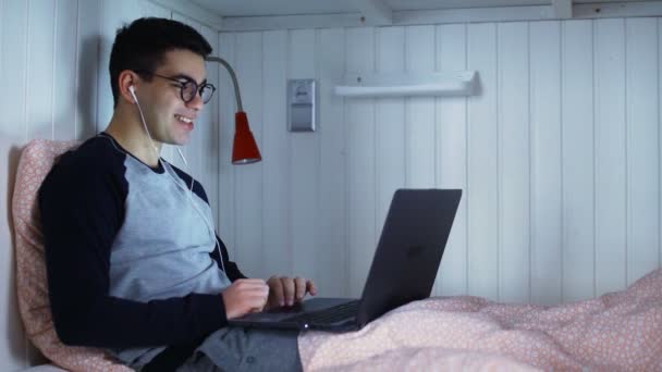 Mann liegt im Bett und spricht mit Webkamera und lächelt — Stockvideo