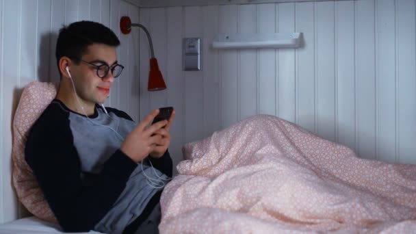 Jeune homme web surf sur son téléphone mobile sur le lit à la chambre de l'auberge — Video