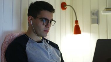 Gözlüklü ve kulaklıklı yakışıklı adam laptopa bak.