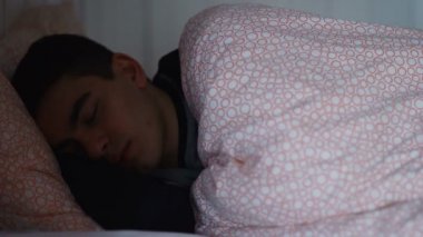 Genç adam gece uyandığında cep telefonuyla evde yatıyor.