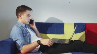 Evdeki yakışıklı mutlu adam, bir süre kanepeye oturur, defterini kullanır ve telefonla konuşur.