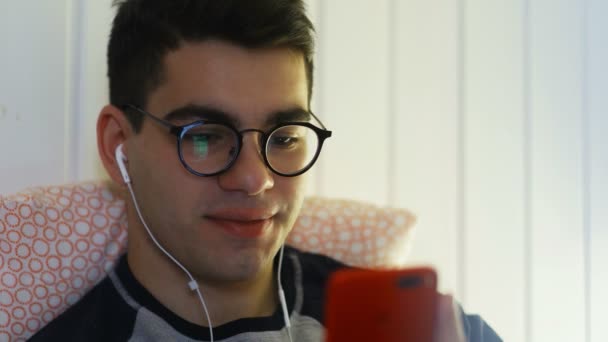 Güzel gülüşü olan çekici ve yakışıklı genç adam sosyal medyada akıllı telefonlardan besleniyor, kıkırdıyor ve uygulamalardaki haberlerden gülüyor. — Stok video