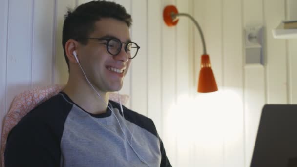 Mladý muž sleduje legrační video na notebooku v posteli v hostelu pokoj — Stock video