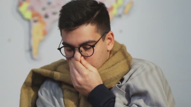 Un hombre con un resfriado se sienta en el sofá y estornuda — Vídeos de Stock