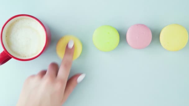 Macarrones o macarones en superficie azul pastel con café en taza roja. — Vídeos de Stock