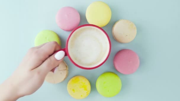Macarrones o macarones en superficie azul pastel con café en taza roja. — Vídeo de stock