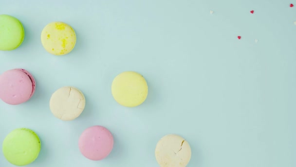 Makronen oder Macarons mit kleinen roten Herzen auf pastellblauer Oberfläche. Nahaufnahme. — Stockvideo