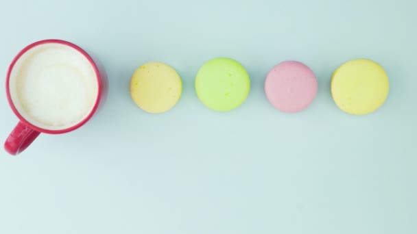 Macarrones o macarones en superficie azul pastel con café en taza roja. — Vídeo de stock