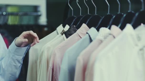 Close-up van vrouw is aanraken hangers met blouses in showroom — Stockvideo