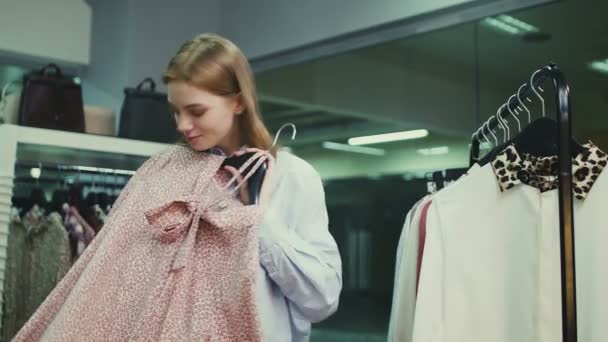 Egy fiatal nő ruhákat próbál fel a ruhaboltban. — Stock videók