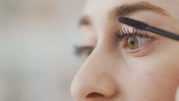 Κοντινό πλάνο του Όμορφη γυναίκα κάνει μακιγιάζ των ματιών από μαύρη μάσκαρα, κοιτάζοντας τον καθρέφτη — Αρχείο Βίντεο