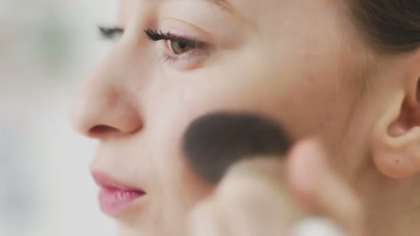 Mujer de belleza aplicando maquillaje. Hermosa chica mirándose en el espejo y aplicando cosméticos con un cepillo grande. La chica se sonroja en los pómulos. Polvo, colorete. — Vídeo de stock